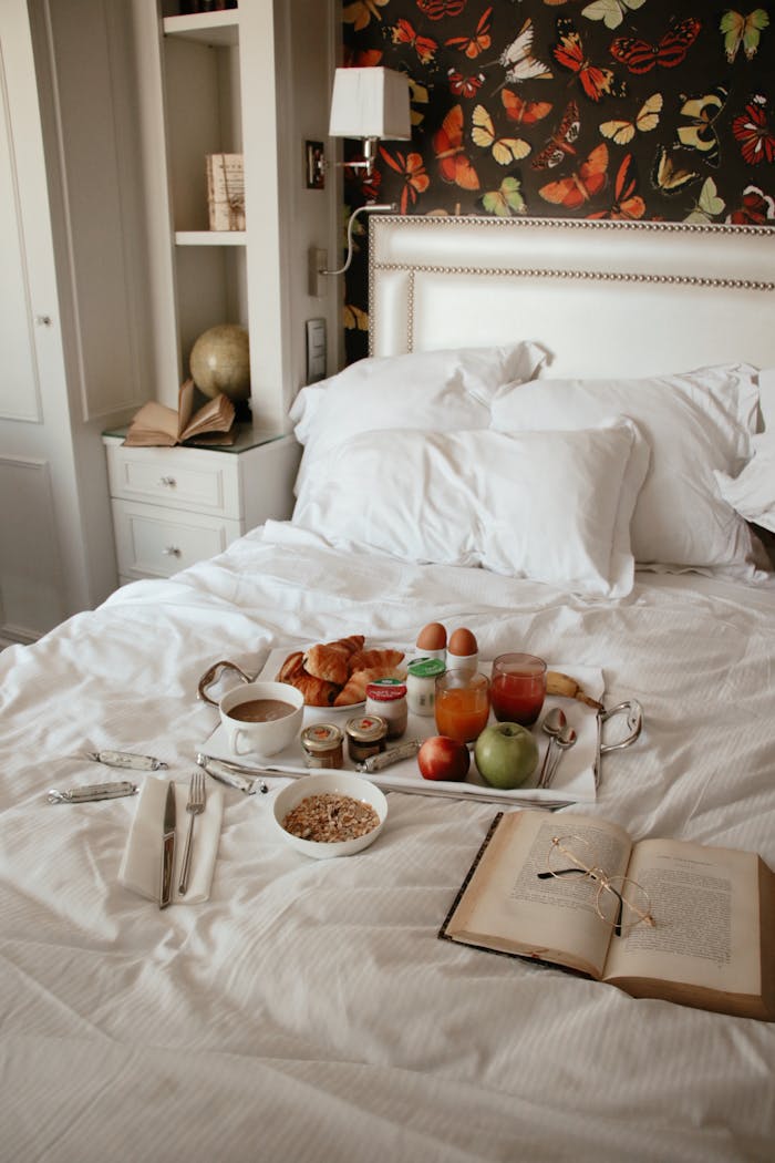 A cozy breakfast in bed with croissants, coffee, and a book in a stylish bedroom setting.