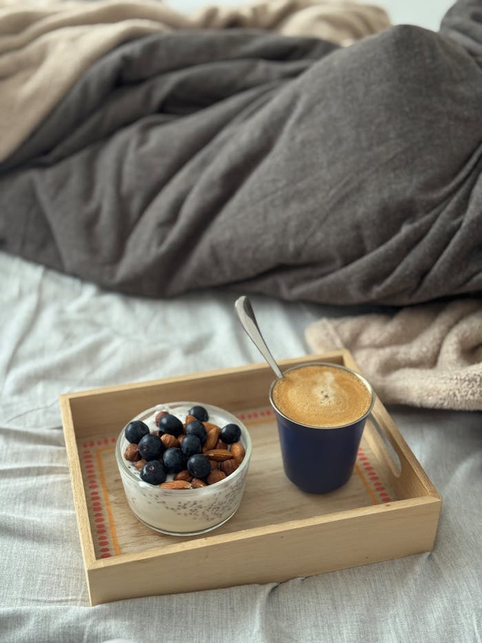 Warm and inviting breakfast set in bed featuring granola with blueberries and a cup of coffee.